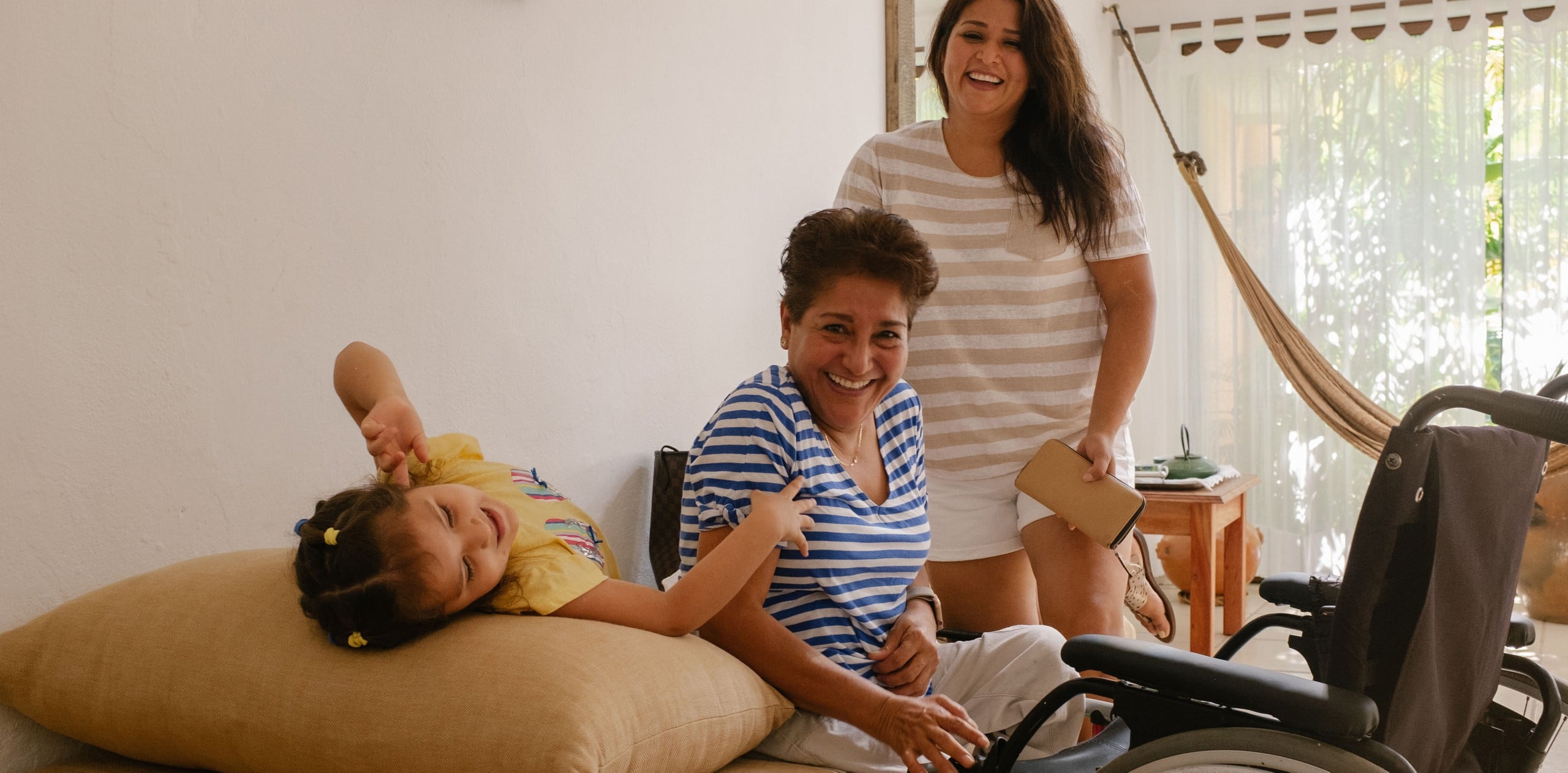 Tres generacions d'una família somriuen i riuen en un allotjament accessible a Airbnb. Davant del membre de més edat de la família hi ha una cadira de rodes.