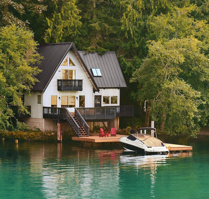 Фото зачехленной лодки, пришвартованной возле двухэтажного дома на берегу озера.