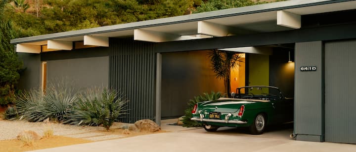 A photo shows the exterior of a single-level desert home with a covered parking spot containing a vintage convertible sports car.