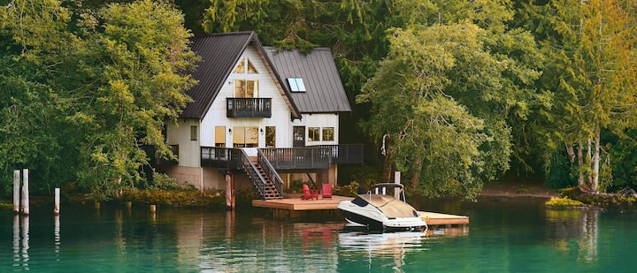 Фото зачехленной лодки, пришвартованной возле двухэтажного дома на берегу озера.