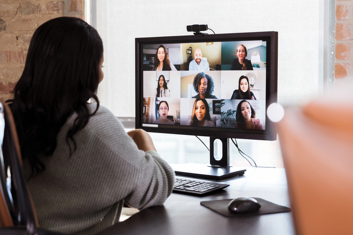 A woman sits at a desk in front of a computer and participates in a video conference online.