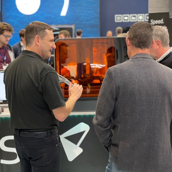 Three men at a tradeshow in discussion. A Formlabs 3D printer is between them in the background.