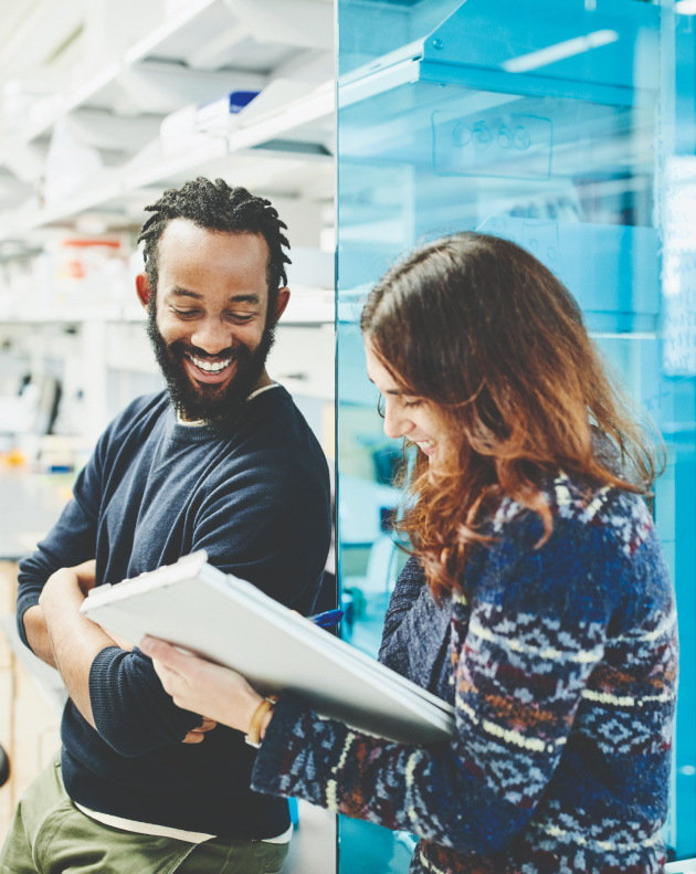 A man and woman smiling and looking down at a writing pad that the woman is holding