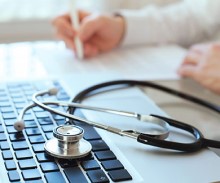 Doctor sitting at a keyboard with stethoscope visible