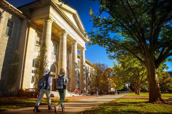 Students with backpacks walk past a building with stone columns