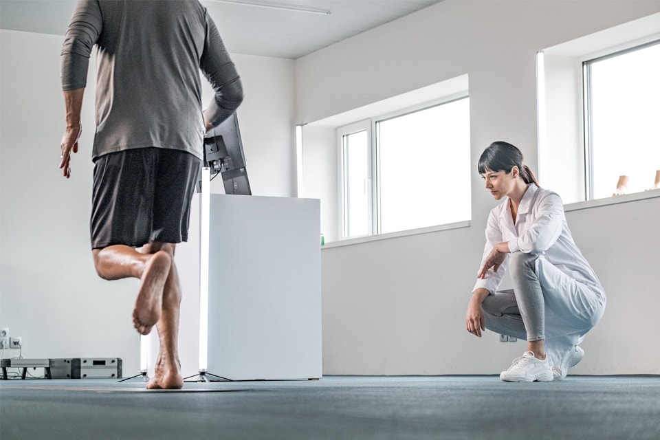 Woman crouching down and observing while a male patient runs over a scanner