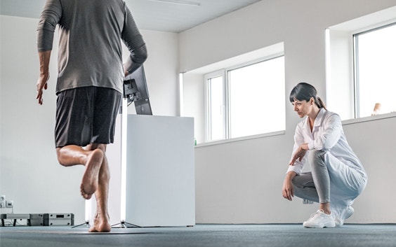 Woman crouching down and observing while a male patient runs over a scanner