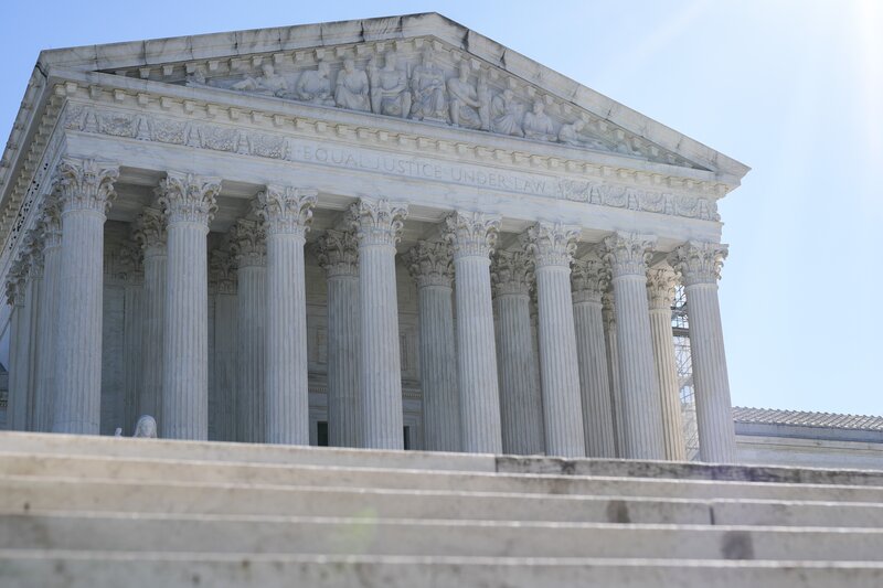 Large white columned building with stairs in the foreground and a light blue sky