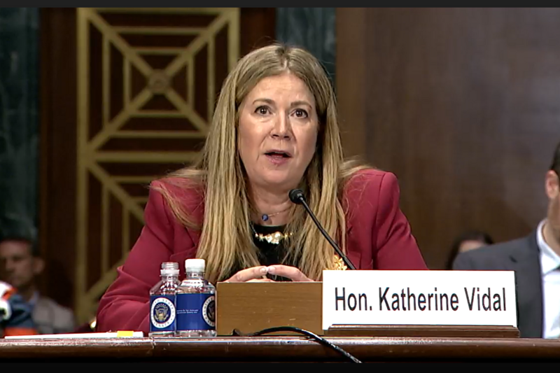 A woman with blonde hair wearing a red blazer testifies before Congress