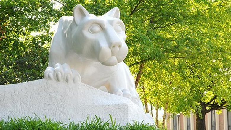 A photo of the Lion Shrine on campus with trees above it and sun shining through the green leaves