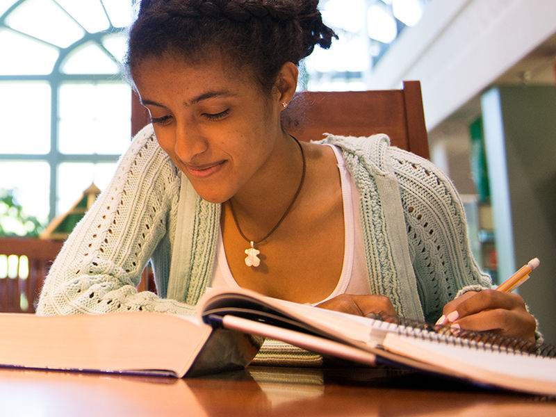 Female student reads book at table in Lilley Library.