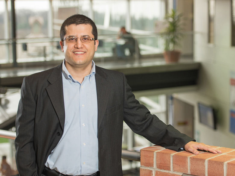 A male faculty member is shown standing by a wall.