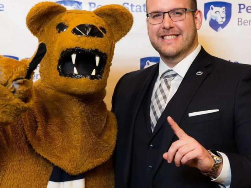 A person stands with the Nittany Lion, both hold up their index fingers