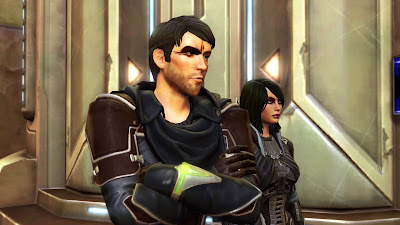 A human male Sith warrior with a face tattoo and a pointy, stubbly chin. He has his arms crossed and dark side Jaesa standing next to him.