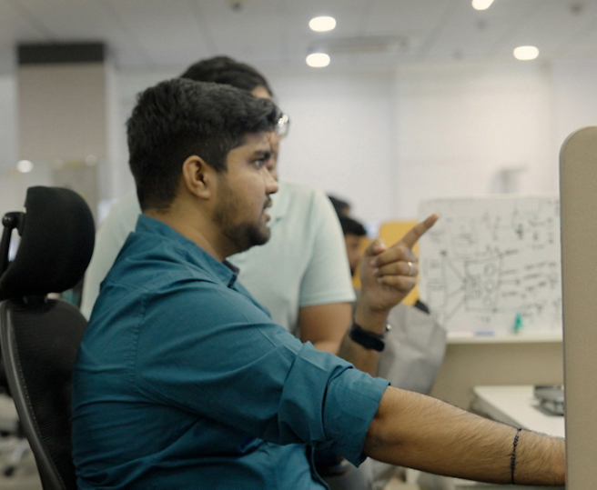 Two men working in an office, one pointing at a computer screen.