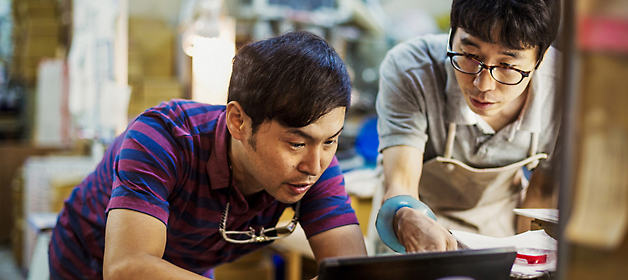 Two craftsmen in a workshop examining a piece closely.