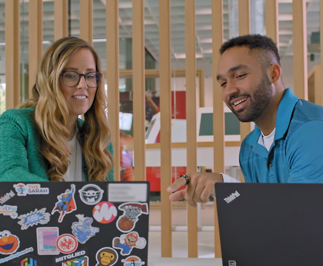 Two professionals discussing work on laptops in a modern office setting.