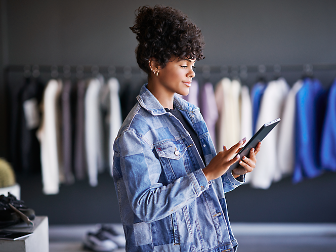 Woman in denim jacket using a tablet in a clothing store.