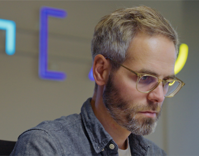 A man in glasses is sitting in front of a computer.