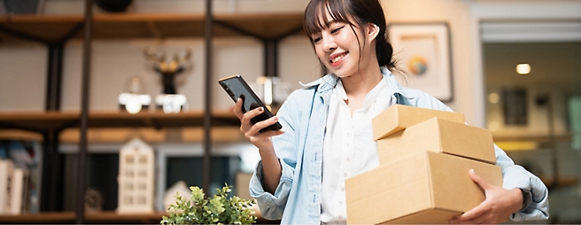 A woman holding a box and a cell phone.