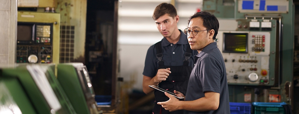 Two people looking at some machine and in that one person is wearing glasses and holding tablet.