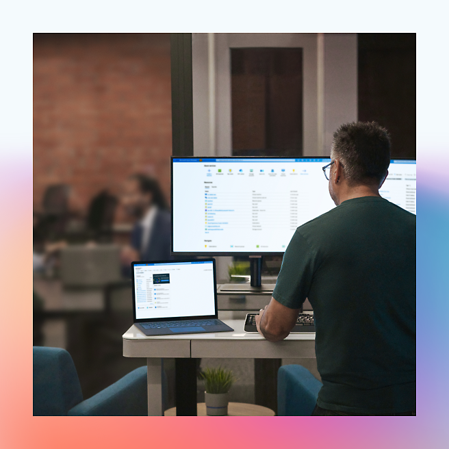 Man working on a computer in a modern office with colleagues in the background.