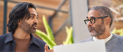 Two men talking to each other while using a laptop.