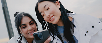 Two women are taking a selfie with their cell phones.