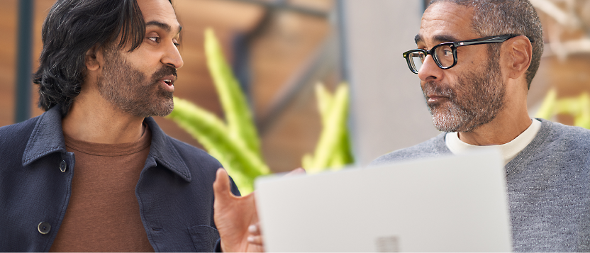 Two men engaged in a conversation behind a laptop in an office environment.