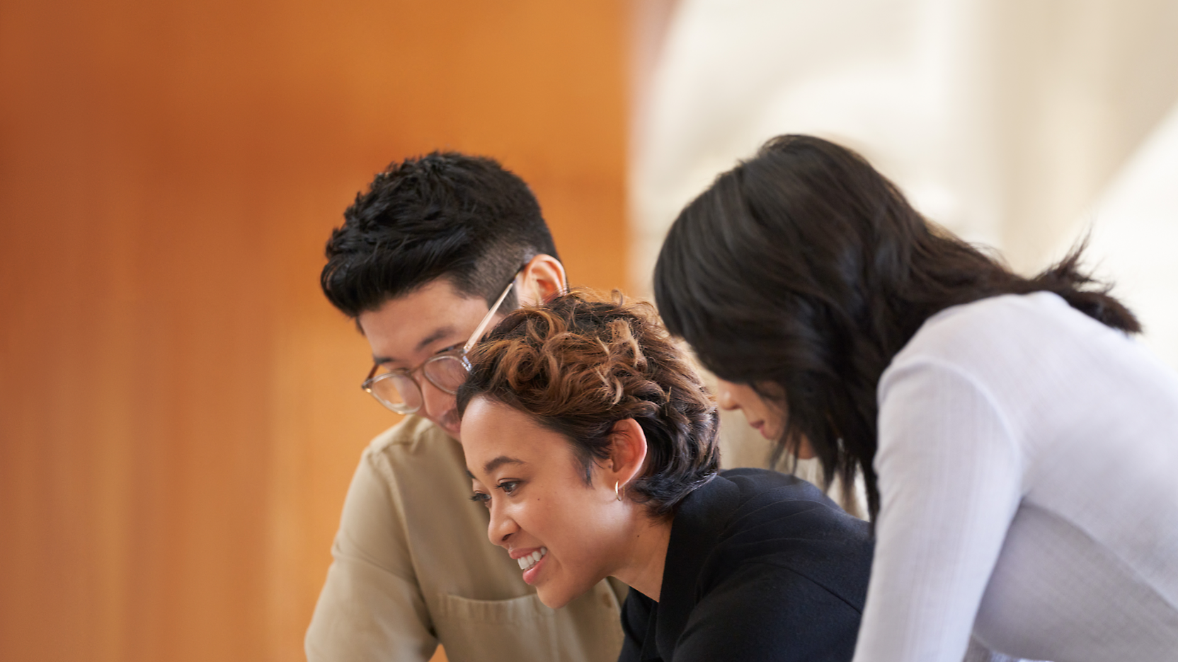 Three colleagues, one woman and two men, collaborating over a document in a well-lit office setting.