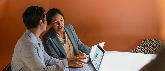 Two people sitting at a table looking at a laptop.