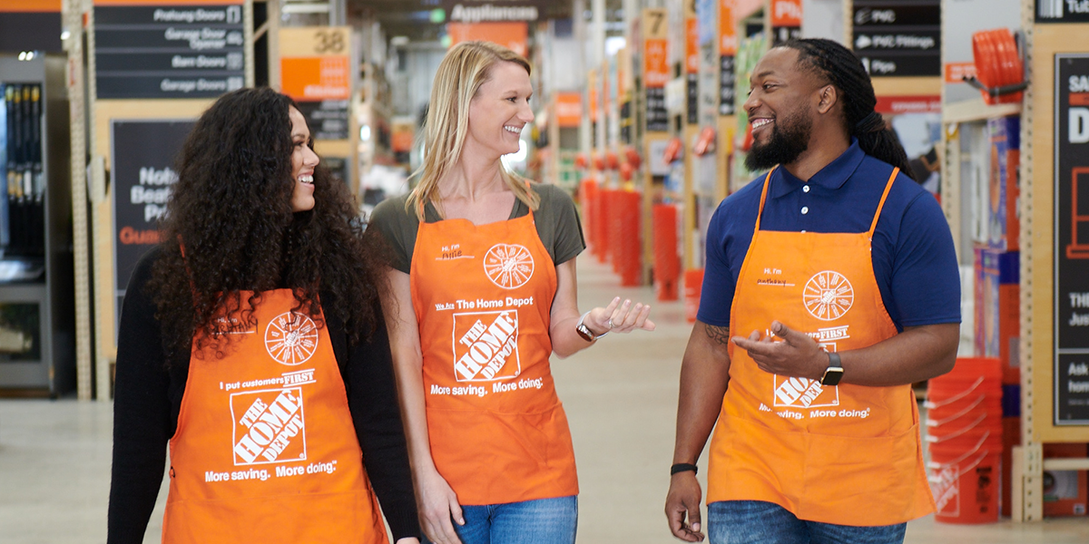 Three Home Depot employees walking through a store aisle while talking and smiling