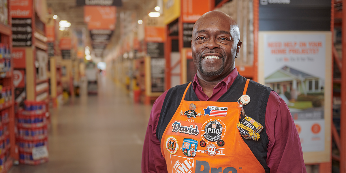 Man posing for photo in an aisle, wearing his Home Depot apron adorned with pins