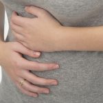 A woman experiencing abdominal pain by covering both hands over her stomach.