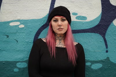 Portrait of smiling woman with pink hair standing against graffiti wall