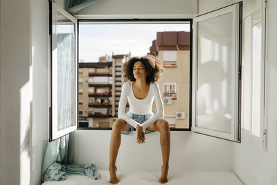 Mixed race woman with eyes closed sitting on window sill at home