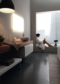 Woman sitting on window sill in bathroom