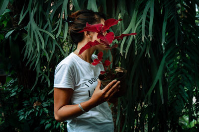 Woman holding plant standing by tree