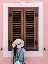 Rear view of woman wearing hat while standing against closed window