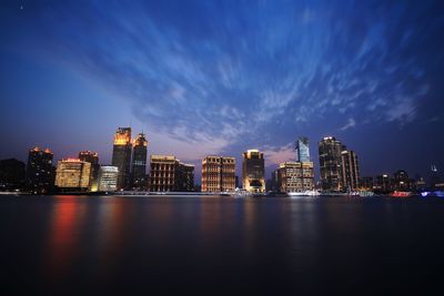 Illuminated buildings by river against sky at night