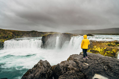 Rear view of woman standing by waterfall