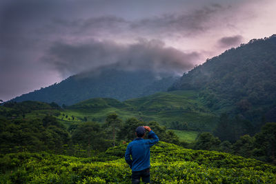 Rear view of man standing on land by mountain against sky