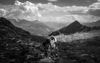 Older man and his grandson standing on mountain against sky