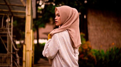 Side view of young woman standing against built structure