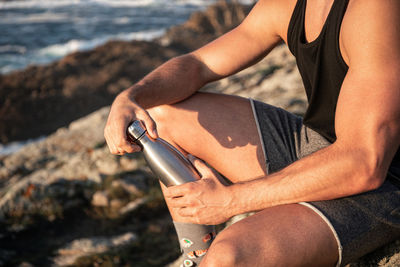 Crop side view of peaceful male sitting on rock on coast and admiring calm seascape at sundown in summer