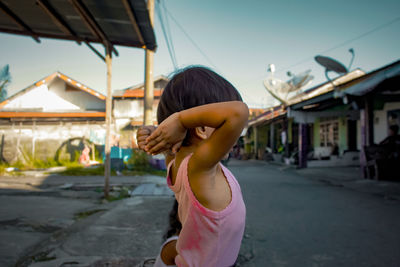 Rear view of woman standing by building against sky