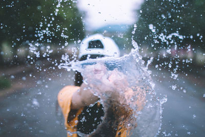 Playful woman splashing water while standing on road