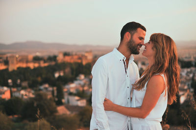 Happy romantic couple kissing against sky during sunset