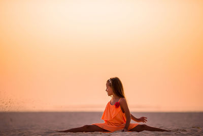 Man sitting on beach against sky during sunset