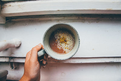 Cropped hand of person holding smoothie over window sill at home